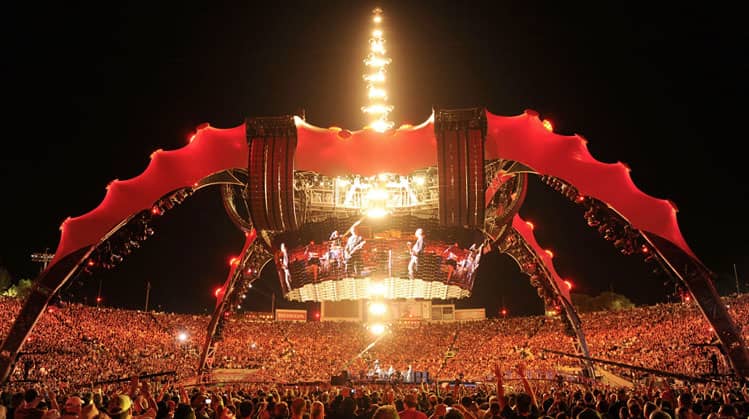 A massive red and black spider-shaped stage structure with glowing lights at its center.